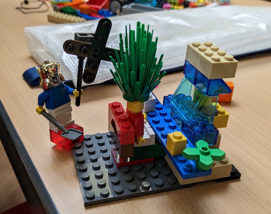 Lego model in which a single minifigure is wearing a metal helmet, holding a shovel and what looks like a large fan.  In front of the minifigure is a construction that a second minifigure seems to be observing with quite shocking, spiked green hair.