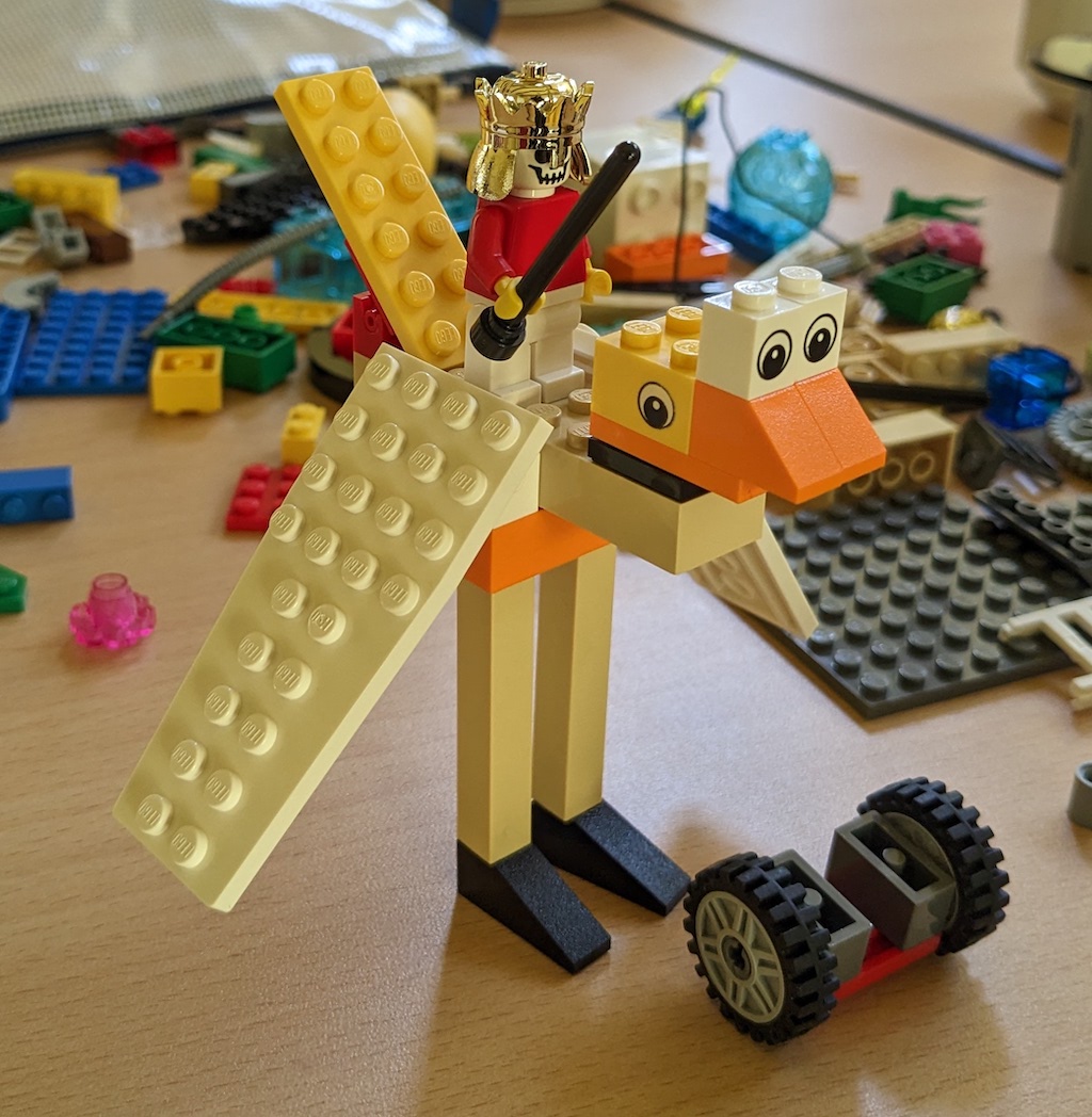 A Lego model of some kind of bird with a gold-helmeted skull-faced minifigure standing on its back, brandishing a black stick.